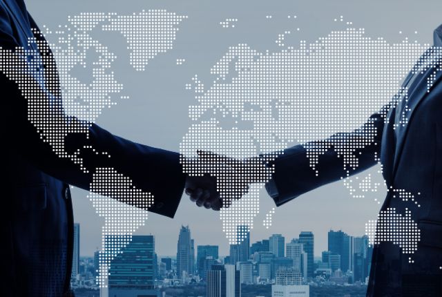世界地図の前でビジネスパーソンが握手する写真。国際ビジネスやグローバルな提携を表すイメージ。