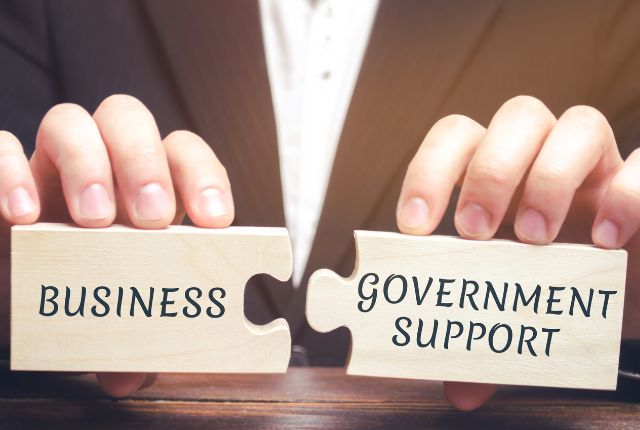 「BUSINESS」と「GOVERNMENT SUPPORT」のパズルをつなぐ手元。企業の外国人採用を支える行政支援や制度連携を示すイメージ。