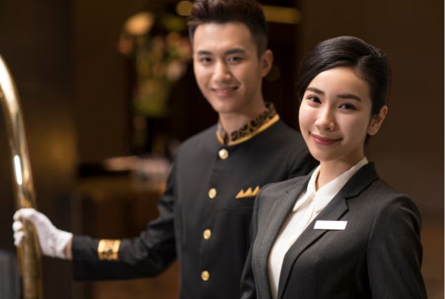 高級ホテルの制服を着たスタッフ2名が笑顔で立つ、上質な接客サービスをイメージさせる写真