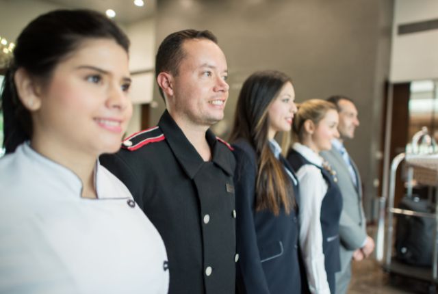 ホテルスタッフ数名が横一列に並び、前を向いて立つ様子。宿泊施設の外国人採用や人材育成を連想させるイメージ。