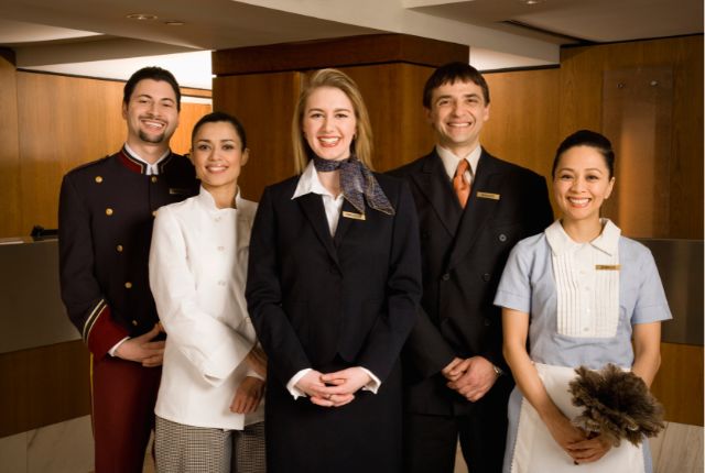 ホテルフロントで働く複数のスタッフが笑顔で並ぶ写真。宿泊業の外国人採用や人材確保に関連するイメージ。