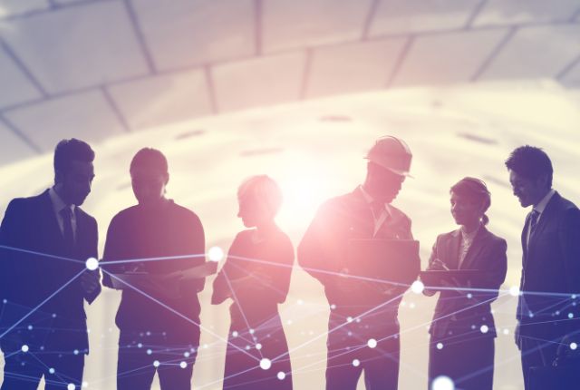 多様な職種の人々が背景の光の中で話し合うシルエット写真。フィリピン人材活用を表すイメージ