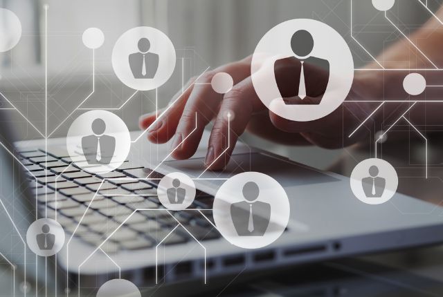 ノートパソコンを操作する手と、人材アイコンのネットワークを重ねた画像。採用管理や人材マネジメントを表現した写真
