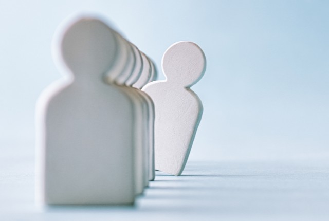 一列に並ぶ人型のオブジェの中で、一体が前に出ている。採用や人材選考、外国人雇用を象徴するイメージ。