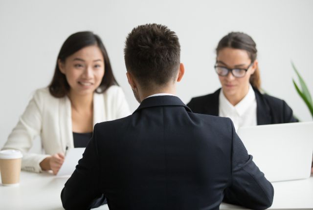 外国人材の雇用面接 面接でスーツ姿の男性応募者が2人の採用担当者と向かい合っている場面。外国人採用や人事面談のイメージ。