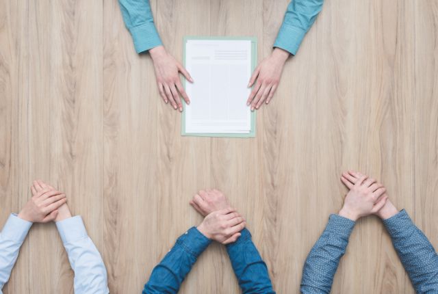 面接や会議の場を示す写真。書類を挟んだファイルを中心に複数の参加者がテーブルに向かい合う様子。