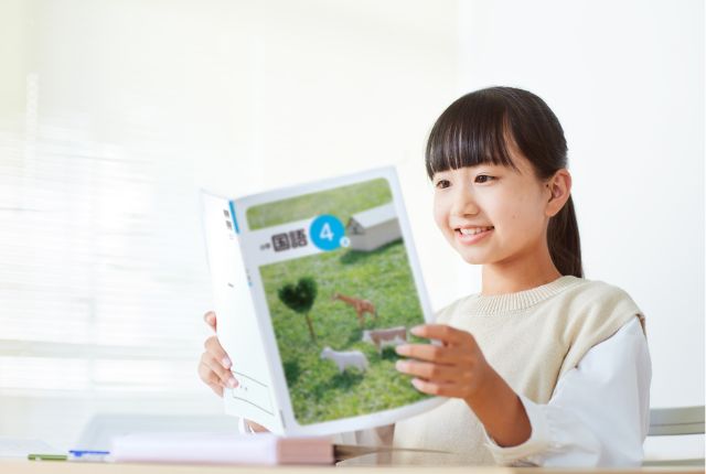 国語の教科書を手に笑顔で勉強する女子小学生。学習意欲や教育現場、外国人子女の日本語教育をイメージ。