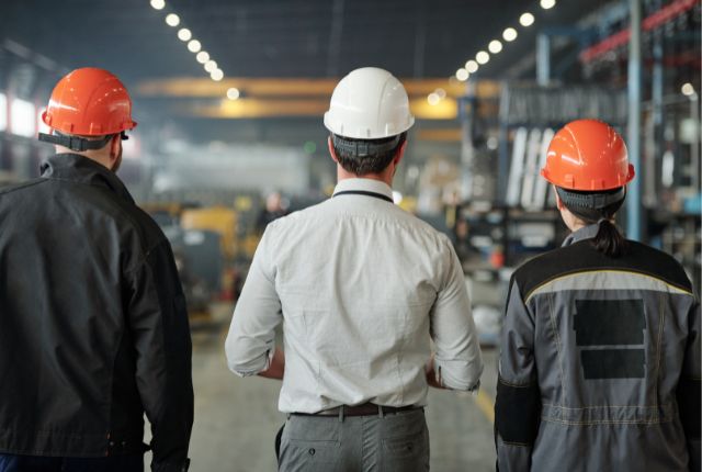製造工場のマネージャー 製造工場で安全ヘルメットを着用した作業員と管理者が現場を確認している様子の後ろ姿。