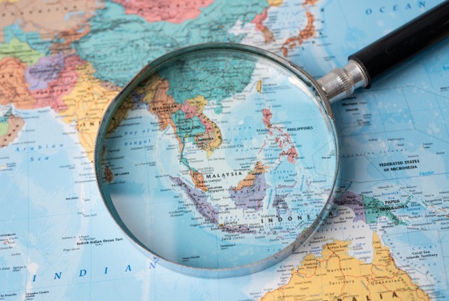 東南アジアの地図を拡大鏡で見る様子。ベトナムやイフィリピンなど外国人技能実習生の送り出し国を示すイメージ。