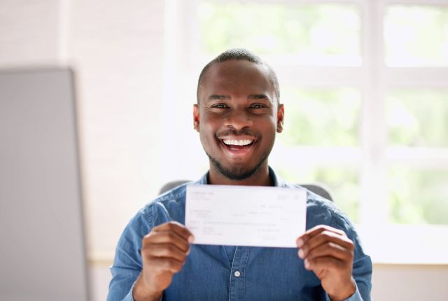 給与明細を手に笑顔を見せる男性。外国人労働者の給与支払い・雇用管理や報酬制度のイメージ。