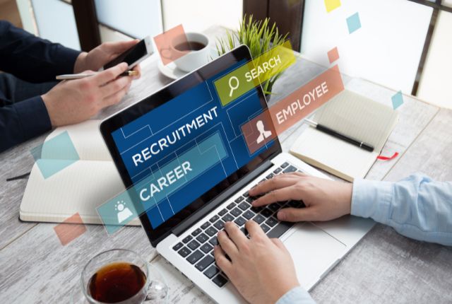 ノートパソコン画面に“RECRUITMENT”“CAREER”“SEARCH”などの文字が浮かぶ。採用活動や求人管理を表すビジネスシーン。