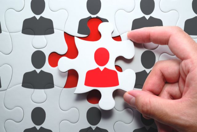 パズルの一片として赤い人物アイコンを選ぶ手の画像。採用活動や適材適所を象徴するイメージ。