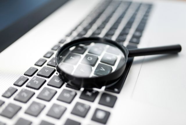 ノートパソコンのキーボードに置かれた虫眼鏡の写真。検索や調査をイメージしたビジュアル素材。