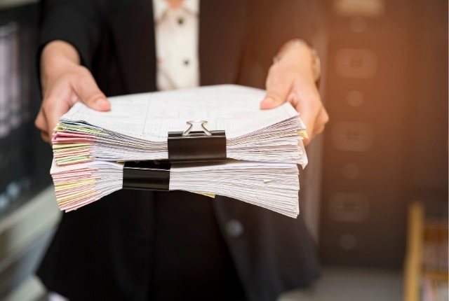 書類の束を差し出すビジネスパーソン。送り出し機関変更に必要な申請書類や監理団体への提出資料をイメージ