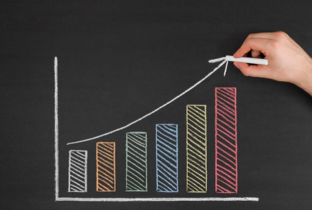 黒板に描かれた上昇するカラフルな棒グラフを手で描いている様子。