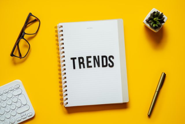黄色い背景にノートと“TRENDS”の文字が置かれた写真。最新トレンドや調査テーマを示すビジュアル。
