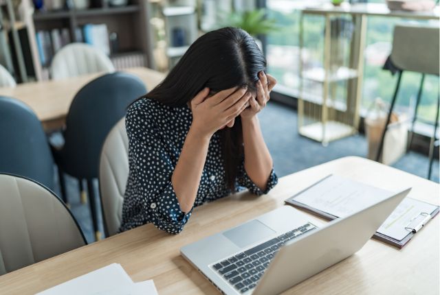 ノートパソコンの前で頭を抱える女性。外国人雇用のトラブルや職場コミュニケーションの課題を表現。