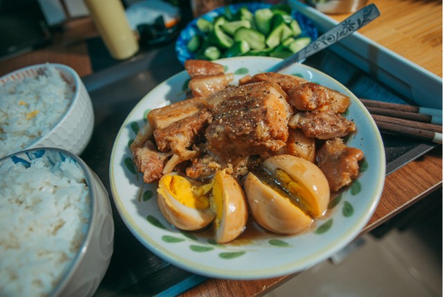 煮卵と豚肉の家庭料理が盛られた皿の写真。フィリピンのご飯と野菜も並ぶ食卓シーン。
