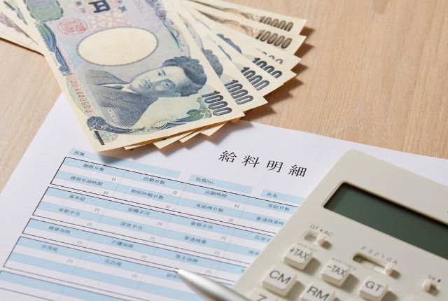日本円の紙幣と給与明細、電卓が置かれた画像。特定技能外国人の給与相場や賃金計算を示すイメージ。