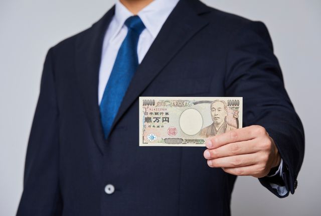 スーツ姿の人物が1万円札を差し出している写真。給与や賃金、支払いに関する内容を示すイメージ。