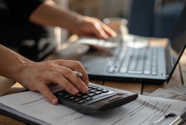 コストの試算 特定技能外国人の受け入れ費用を計算するイメージ。書類作成とコスト管理を示す電卓とパソコンの作業風景。