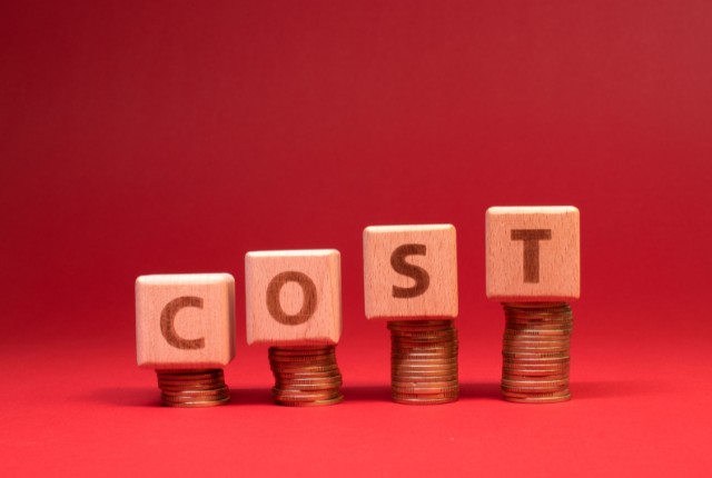 固定費の計算 赤い背景にコインを積み上げ、その上に「COST」の木製ブロックを並べた画像。費用やコスト計算を示すイメージ