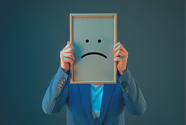 特定技能外国人の不満 悲しい顔のボードを掲げる人物のイメージ写真。ストレスや不満、悩みを象徴するビジュアル。