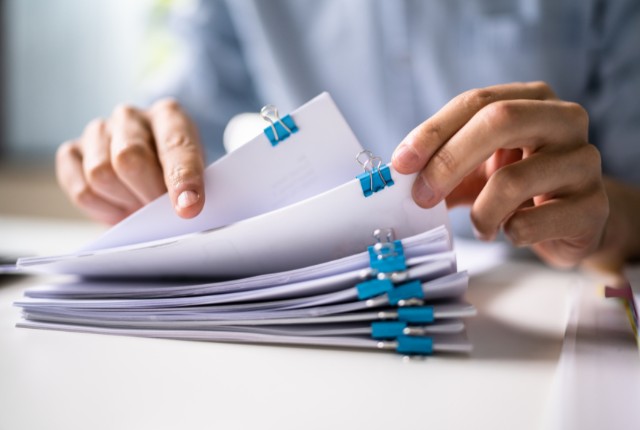 申請書類の確認 複数の書類を手で確認する様子。申請や手続きで必要な資料を整理しているイメージ画像。