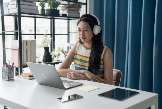 外国人社員がオンラインで日本語学習を進める様子。ヘッドホンをつけてパソコンで教材に取り組む女性学習者の姿。