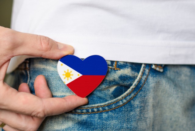 フィリピン国旗のハート型バッジをジーンズに添える手の写真。フィリピンへの愛情や文化を象徴するシーン。