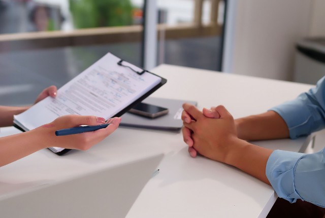 特定技能外国人との定期面談 面談で書類を確認する様子。雇用手続きや相談対応、外国人労働者のサポート場面をイメージした写真。
