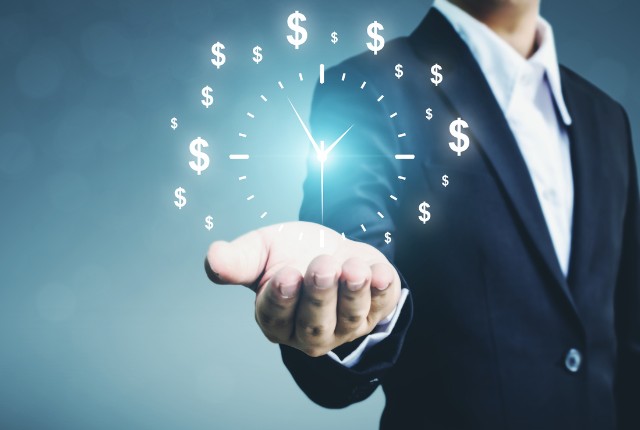 時間とコスト スーツの人物が時計とドル記号のホログラムを示すイメージ。費用や手続き時間を表すビジネス概念の画像。